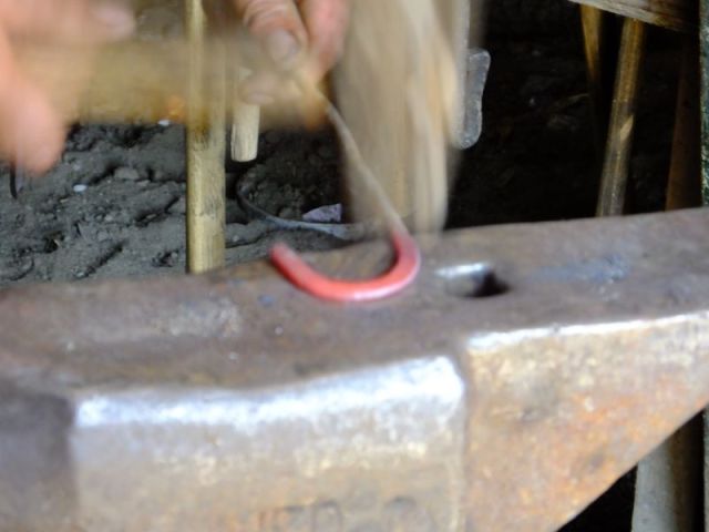 Flattening the hot metal with a hammer which only shows up as a blur